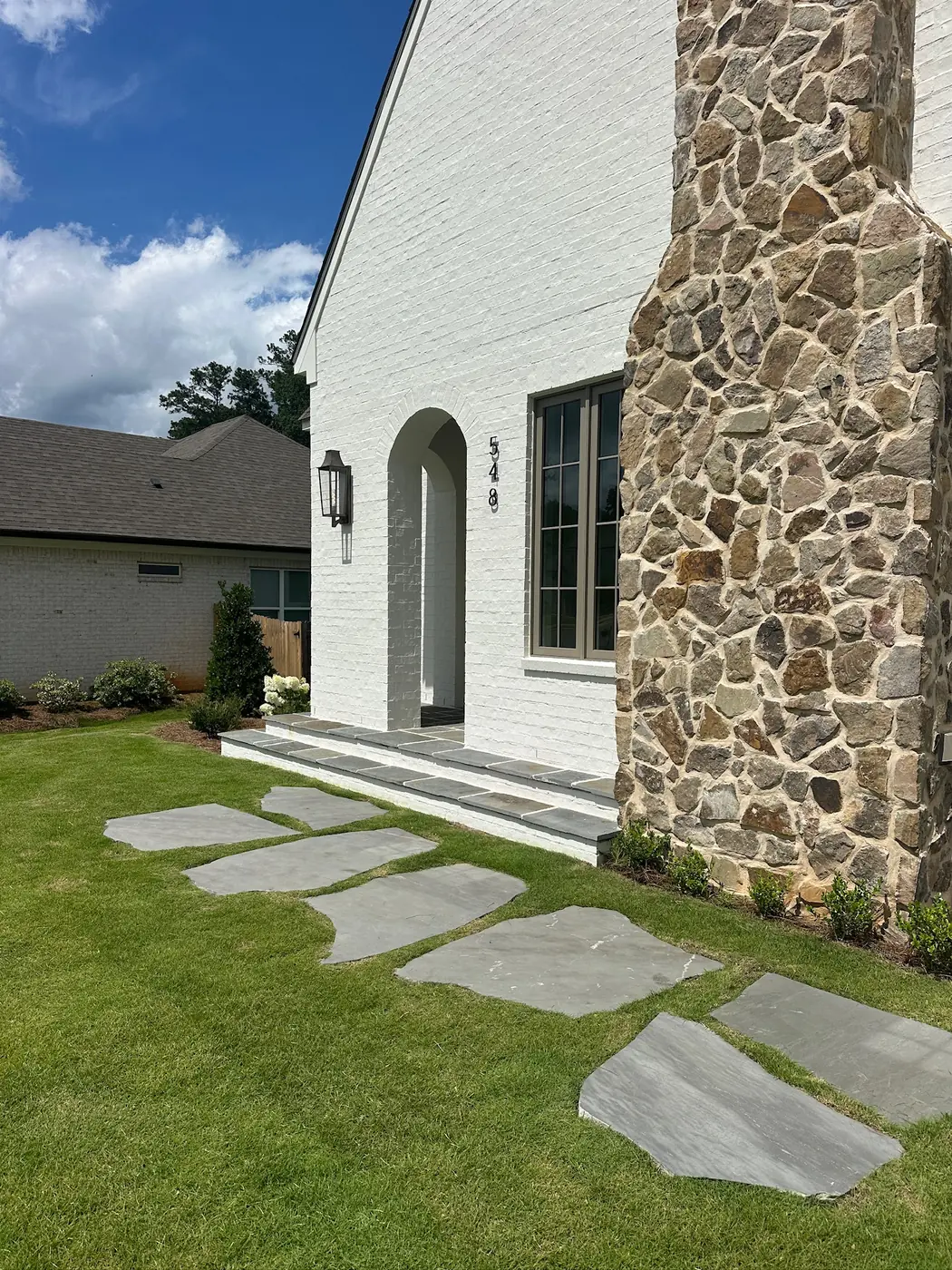 Clean lawn and flagstone walkway at a white home with a stone chimney