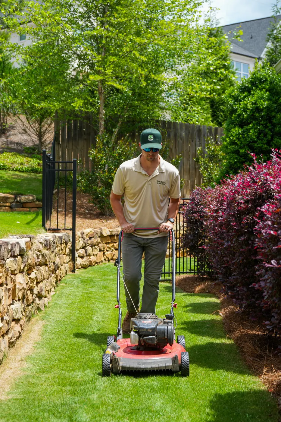 Push mowing crisp stripes beside a stone retaining wall