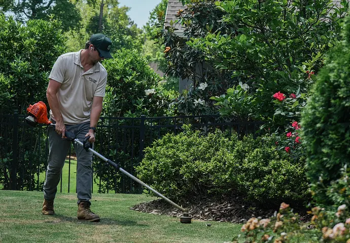 Rolling Lawns owner edging along garden beds with a string trimmer